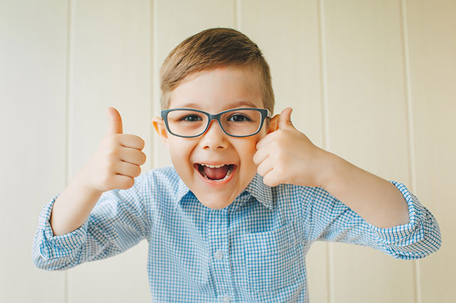 pediatric boy with glasses giving two thumbs up and smiling